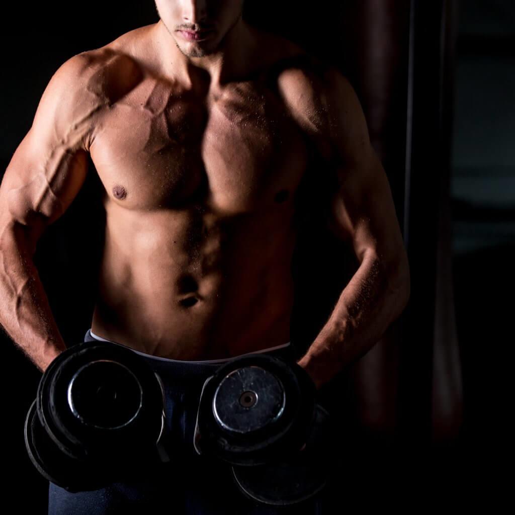 Young attractive caucasian bodybuilder sportsman working out with dumbbells in gym, doing training for shoulder muscles, close up