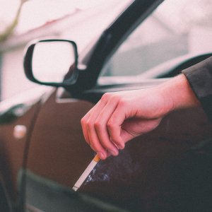 a driver's arm hanging out the car window holding a cigarette