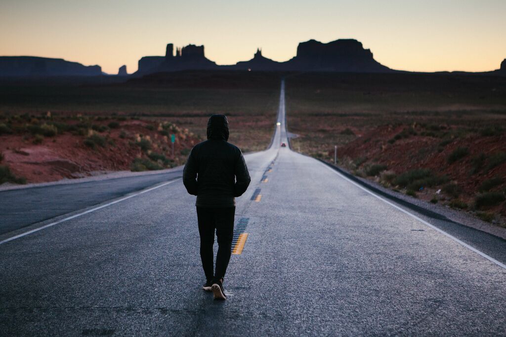 a solitary figure walking alone down a deserted highway in the desert